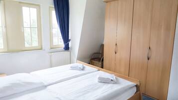 Ein Hotelzimmer mit zwei Betten, einem Kleiderschrank, einer Heizung und einem Fenster mit Vorhängen.