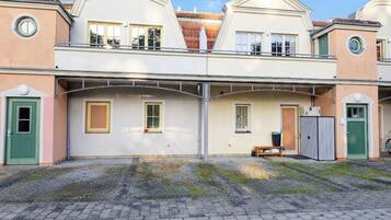A two-story building with a central balcony, a small bench, and a trash bin.