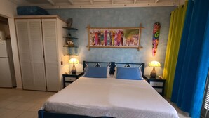 A bedroom with a bed, two nightstands, a wardrobe, and a wall with surfboards. - Green Garden Apartment at Blue Ocean Cottage in Silver Sands (Silver Sands)