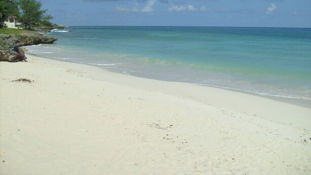 A beach with clear turquoise water, white sand, and a few people on the shore. - Green Garden Apartment at Blue Ocean Cottage in Silver Sands (Silver Sands)