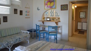 A room with a sofa, two chairs, a table, and a small kitchen area with a toaster. - Green Garden Apartment at Blue Ocean Cottage in Silver Sands (Silver Sands)