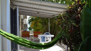 A covered outdoor seating area with a hammock, chairs, and a table. - Green Garden Apartment at Blue Ocean Cottage in Silver Sands (Silver Sands)