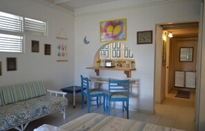 A room with a sofa, two chairs, a table, and a small kitchen area with a toaster. - Green Garden Apartment at Blue Ocean Cottage in Silver Sands (Silver Sands)