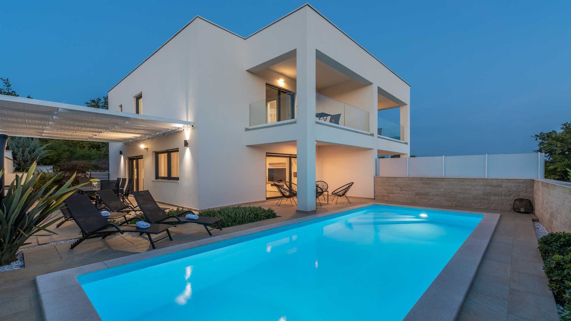 Ein modernes, zweistöckiges Haus mit Swimmingpool, Sitzgelegenheiten im Freien und einer überdachten Terrasse.