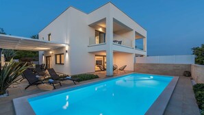 A modern two-story house with a swimming pool, outdoor seating, and a covered patio area.