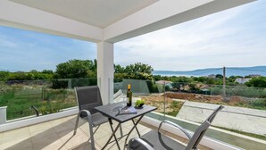 A balcony with a table, chairs, a bottle of wine, and a bowl of grapes.