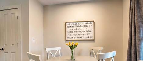 A dining area with a round table, white chairs, and a vase of yellow flowers.