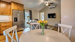 A modern kitchen with wooden cabinets, a stainless steel refrigerator, a dining table with a vase of flowers, and a ceiling fan.