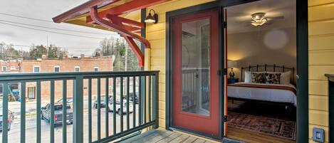 A room with a bed, a wooden deck, a red awning, and a view of parked cars.