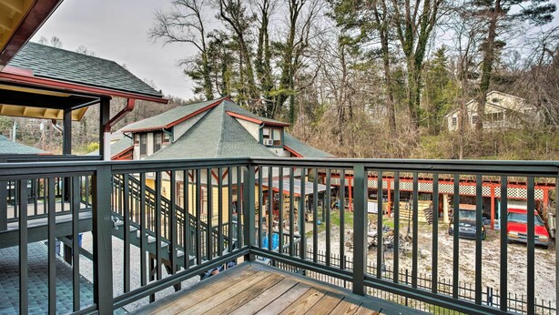 A wooden deck with a metal railing, a covered area with a green roof, and a view of a building surrounded by trees.