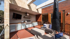 An outdoor kitchen area with a flat-screen TV, built-in grill, and seating with cushions. - Pet Friendly - Garden Elegance in Blairgowrie (Blairgowrie)