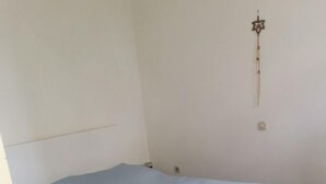 Um quarto com uma cama de solteiro, luminária na parede e uma porta.