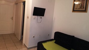 Quarto com uma cama, televisão fixada na parede e uma porta.