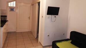 Quarto com uma cama, televisão na parede, uma porta e uma janela pequena.