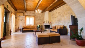 A spacious living room with a high wooden ceiling, stone walls, and a fireplace. There are two sofas, a coffee table, and a TV stand. - Kissamos rental villa with private pool (Kissamos)