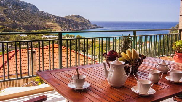 A wooden table with white teacups and a pitcher, a bowl of fruit, and a view of the sea and hills. - Kissamos rental villa with private pool (Kissamos)