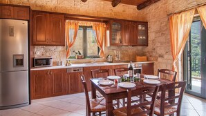 A rustic kitchen with wooden cabinets, a built-in microwave, and a dining area with a wooden table and chairs. - Kissamos rental villa with private pool (Kissamos)