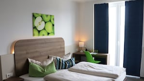A hotel room with a bed, a desk, a chair, a lamp, and a window with curtains. - Hotel M24 (Vechta)