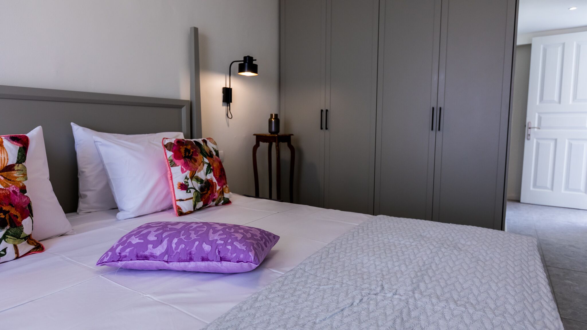 Habitación de hotel con cama, almohadas, mesita de noche, lámpara y armario.