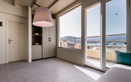 A modern bedroom with a large window, a ceiling lamp, and a view of a cityscape and mountains.