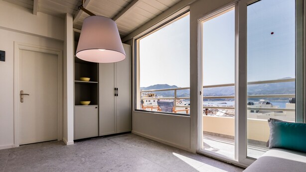 Quarto moderno com uma janela grande, uma luminária no teto e vista para a paisagem urbana e montanhas.