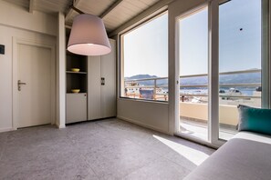 A modern bedroom with a large window, a ceiling lamp, and a view of a cityscape and mountains. - Lemon Tree House (Karpathos)