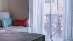 Quarto com cama, sofá com almofadas estampadas e vista para um pátio externo.
