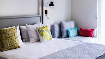 A neatly made bed with white bedding and multiple pillows in various patterns.
