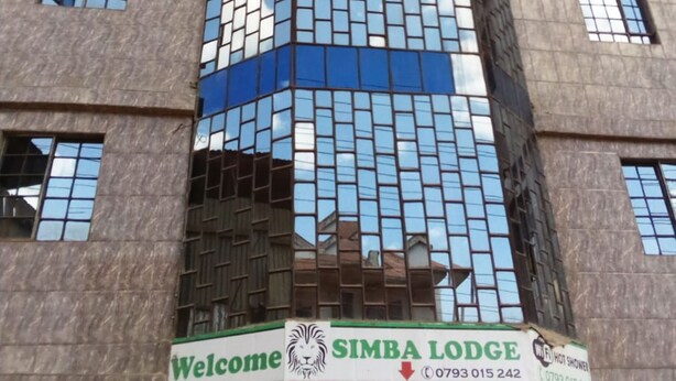 A multi-story building with a modern glass facade, a 'Welcome' sign, and a 'SIMBA LODGE' sign with contact numbers. - Simba Lodge (Embu)
