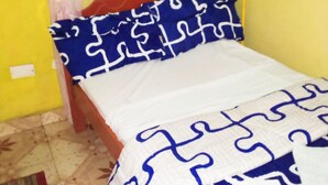 A small, single-bed room with a wooden headboard, a patterned bedspread, and yellow walls. - Simba Lodge (Embu)