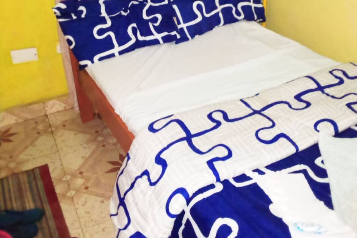 A small, single-bed room with a wooden headboard, a patterned bedspread, and yellow walls.