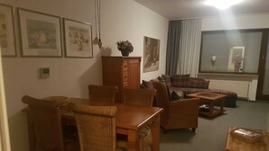 Uma sala de estar acolhedora com uma mesa de jantar, cadeiras de vime, um sofá e uma mesa de centro.