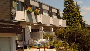 Um edifício moderno de dois andares, com varanda, janelas amplas e antena parabólica.