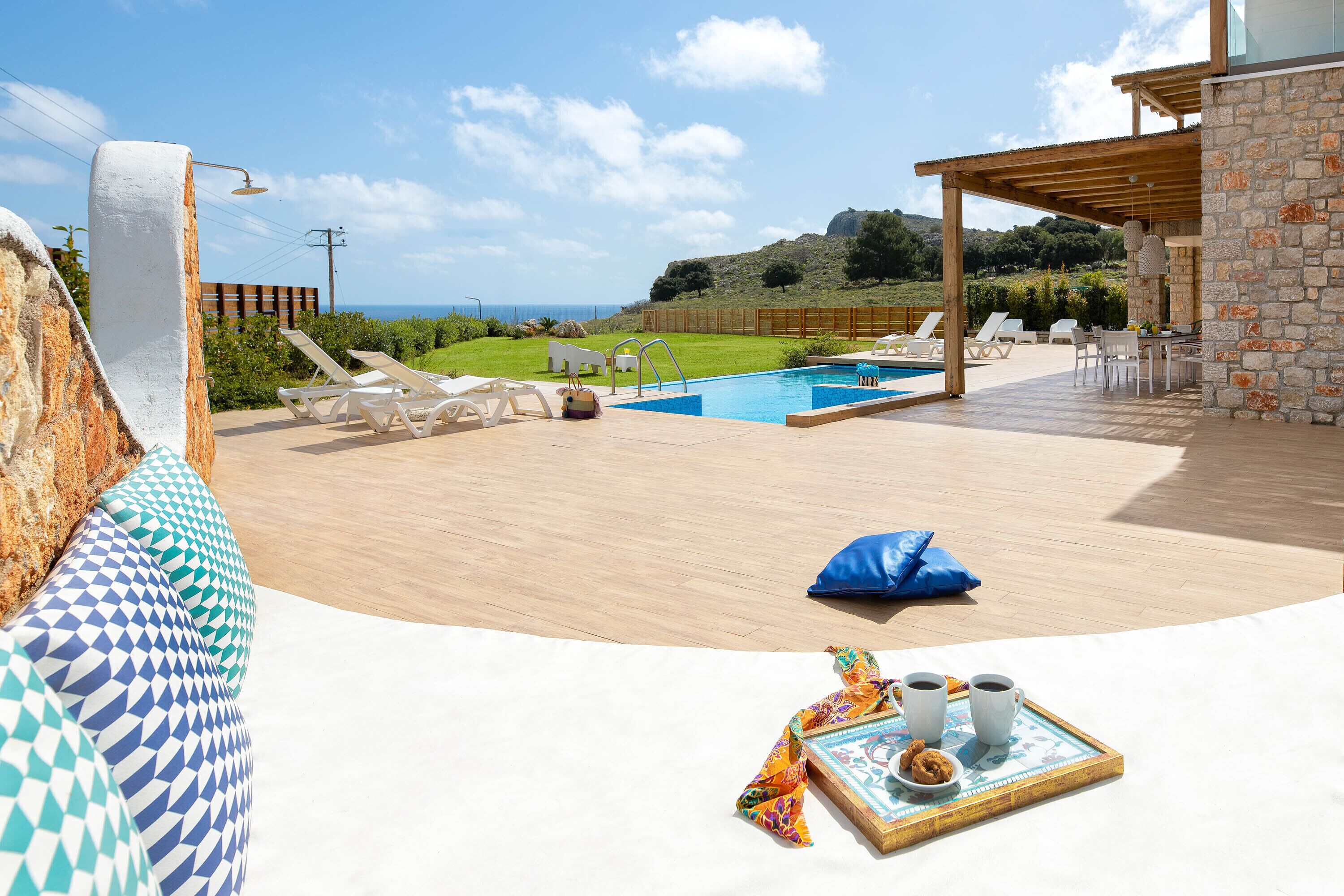 Area piscina con lettini, un solarium in legno e un edificio in pietra con vista sul mare.