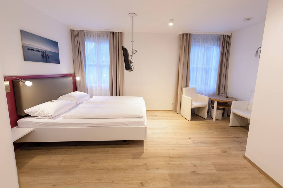 A hotel room with a bed, a desk, a chair, and a television mounted on the wall.