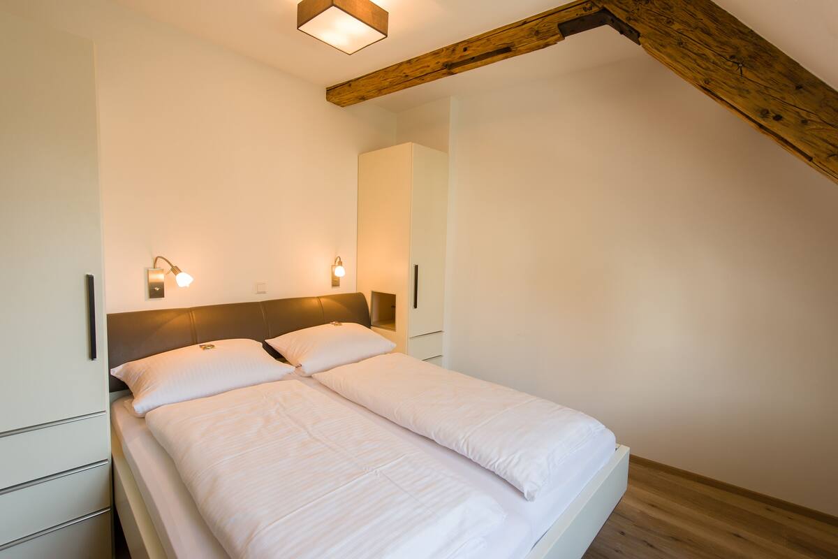 A single bed with white bedding in a room with wooden beams and two wall-mounted lights.