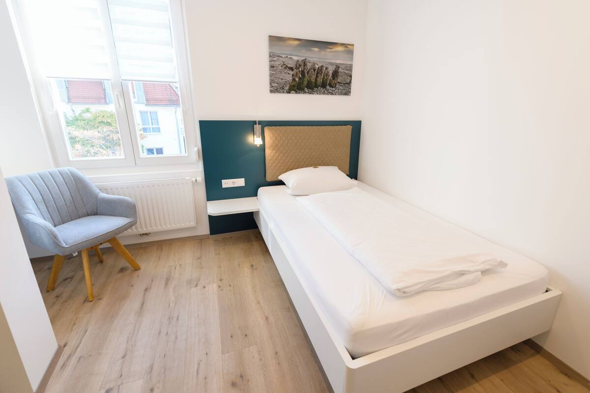 A bedroom with a bed, a chair, a window, and a wall-mounted picture.
