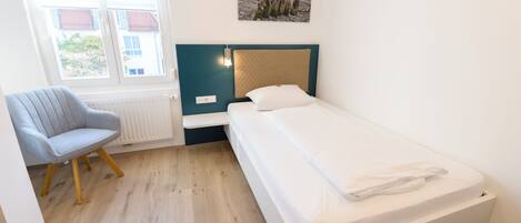 Une chambre à coucher avec un lit, une chaise, une fenêtre et un tableau accroché au mur.