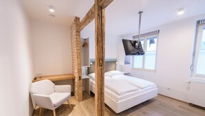 Un dormitorio moderno con techo de madera, cama blanca, un escritorio y una silla.