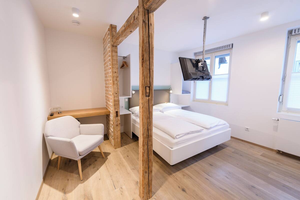 A modern bedroom with a wooden ceiling, a white bed, a desk, and a chair.