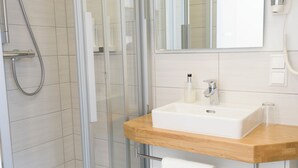 Un baño moderno con ducha envuelta en vidrio, un lavamanos blanco y encimera de madera, y un espejo sobre el lavamanos.