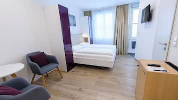 Habitación de hotel con cama, dos sillones, un escritorio con teclado, televisor y ventana con cortinas.