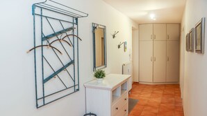 Un couloir avec une armoire blanche, un miroir et un étagère en métal.