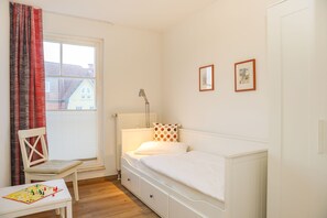 Une chambre avec un lit simple, une chaise, une table avec un jeu de société et une fenêtre avec des rideaux.