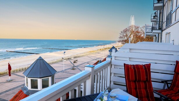 Un balcon avec vue sur la plage et l’océan. On y trouve une table avec une chaise et un petit kiosque.