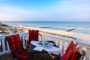 Une terrasse avec une table dressée pour deux personnes, donnant sur une plage avec une jetée.