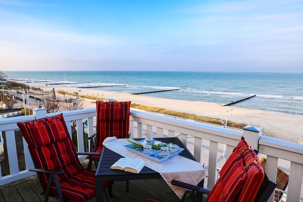 A deck with a table set for two, overlooking a beach with a pier.