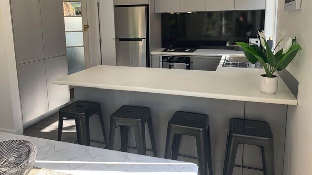 Una cocina moderna con una isla central, taburetes de bar, electrodomésticos de acero inoxidable, iluminación colgante y una planta en maceta.