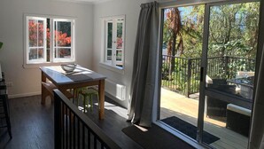 Una habitación con mesa de comedor, sillas, vista a árboles a través de una ventana y un balcón con mobiliario exterior.