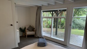 Una habitación con cama, una silla, un ventanal y vistas al verdor exterior.